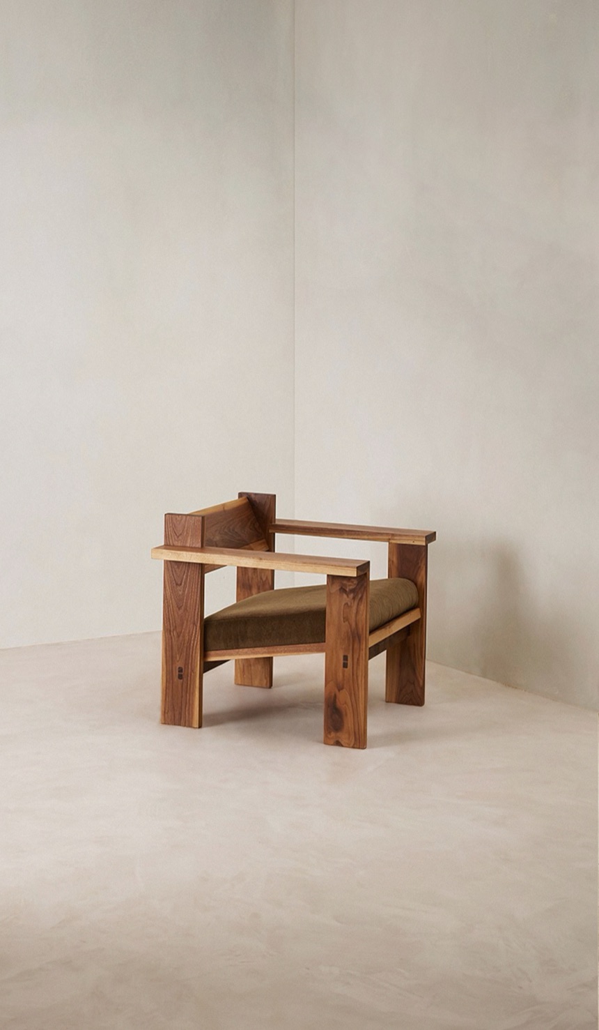 The Ritual Chair — a handcrafted timber armchair with an olive cushion, in a warm plaster-walled room.